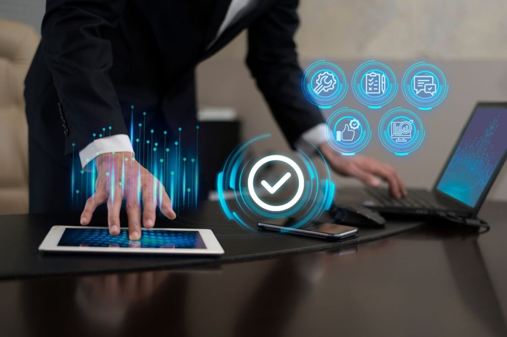 A person in a suit leans over a tablet on a desk, with a holographic checkmark icon above their hand, indicating the completion of annual compliance for a public limited company. Nearby are a laptop, smartphone, and holographic icons representing various digital functions including communication, checklist, and security.