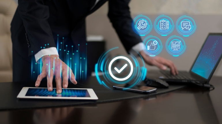 A person in a suit leans over a tablet on a desk, with a holographic checkmark icon above their hand, indicating the completion of annual compliance for a public limited company. Nearby are a laptop, smartphone, and holographic icons representing various digital functions including communication, checklist, and security.