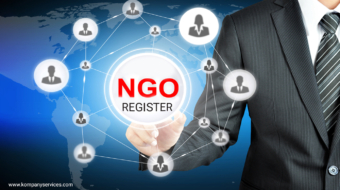 A businessman in a suit points at a digital interface displaying "NGO REGISTER" in red text, symbolizing NGO registration. Surrounding the text are icons of people connected in a network, with a world map backdrop. The URL www.kompanyservices.com is visible at the bottom left corner.